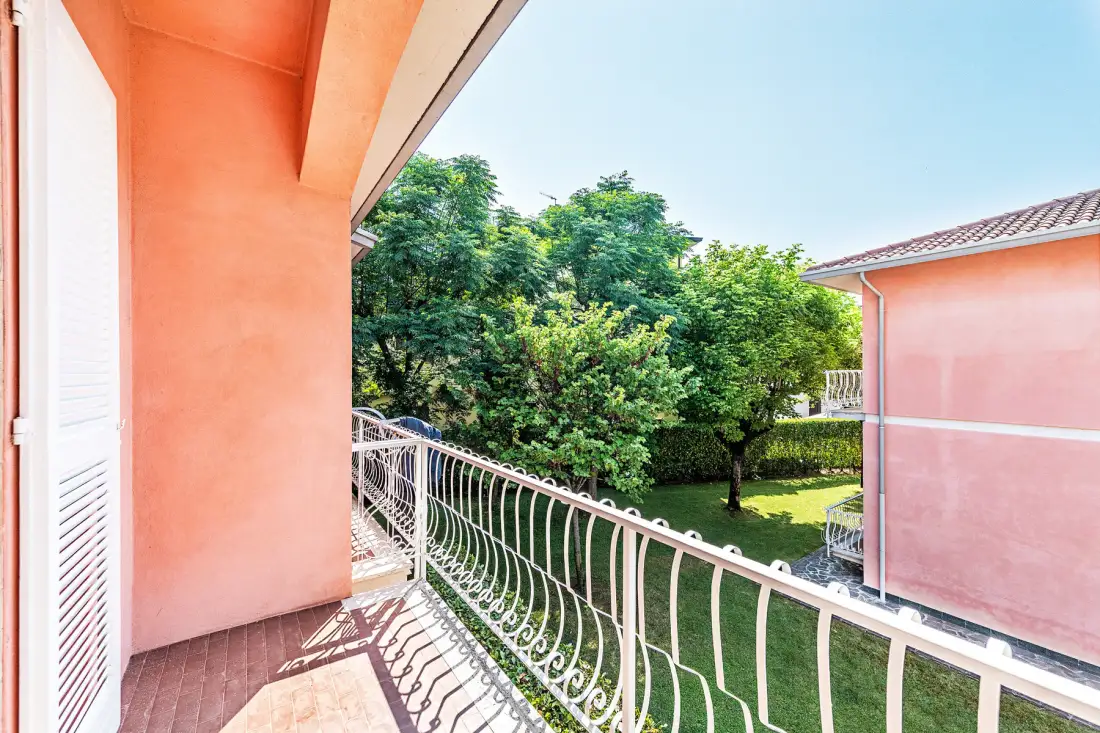 A balcony overlooks a green garden with trees and lawn.