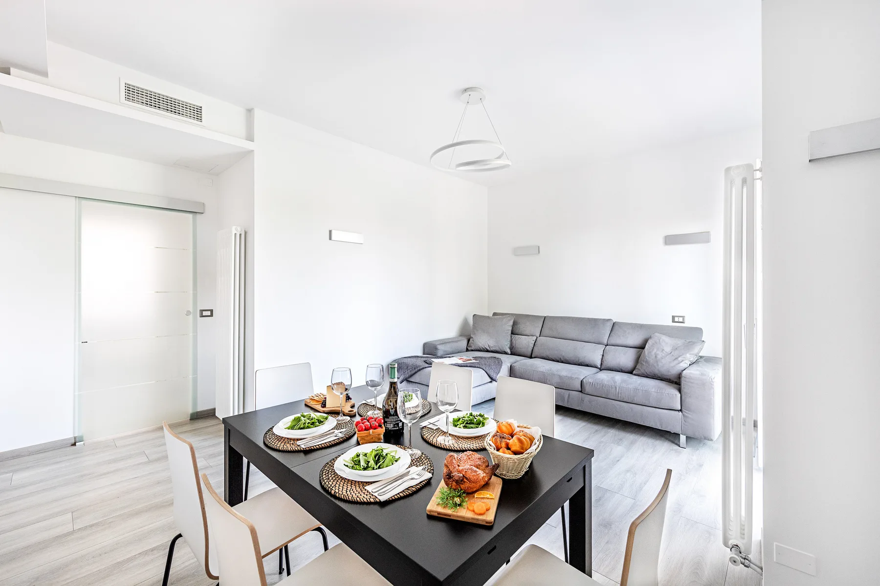 A bright living and dining area with a gray sofa and a set dining table.