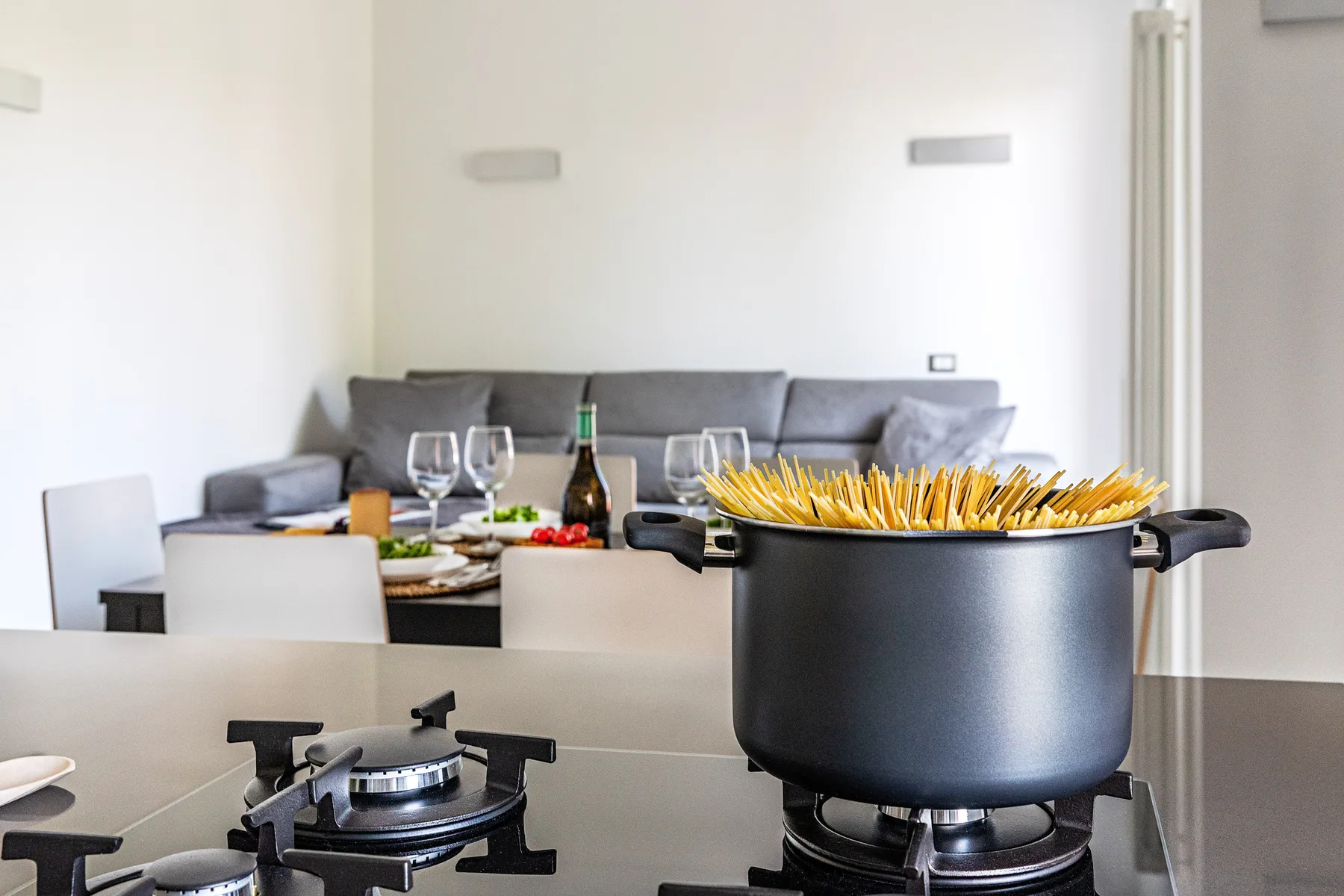 A kitchen counter with a large pot on the stovetop and a dining table behind it.