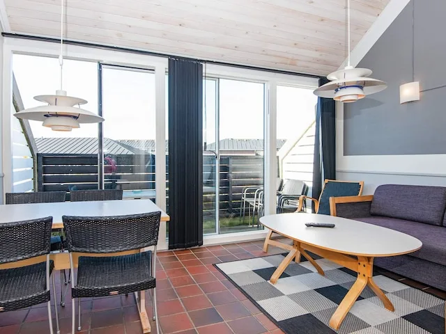 A bright living and dining area with a table, seating, and large windows.
