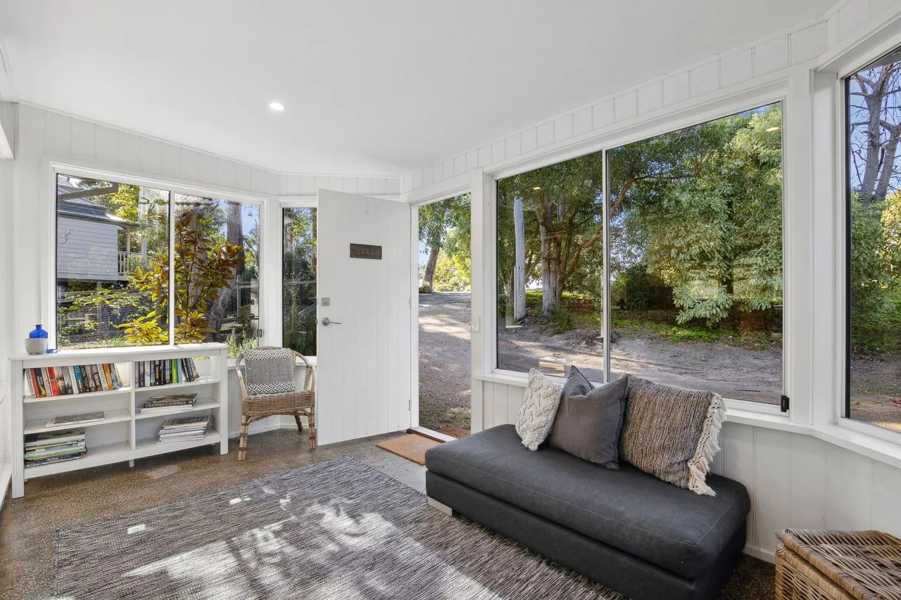 A bright sunroom with a dark sofa and large windows overlooking trees.