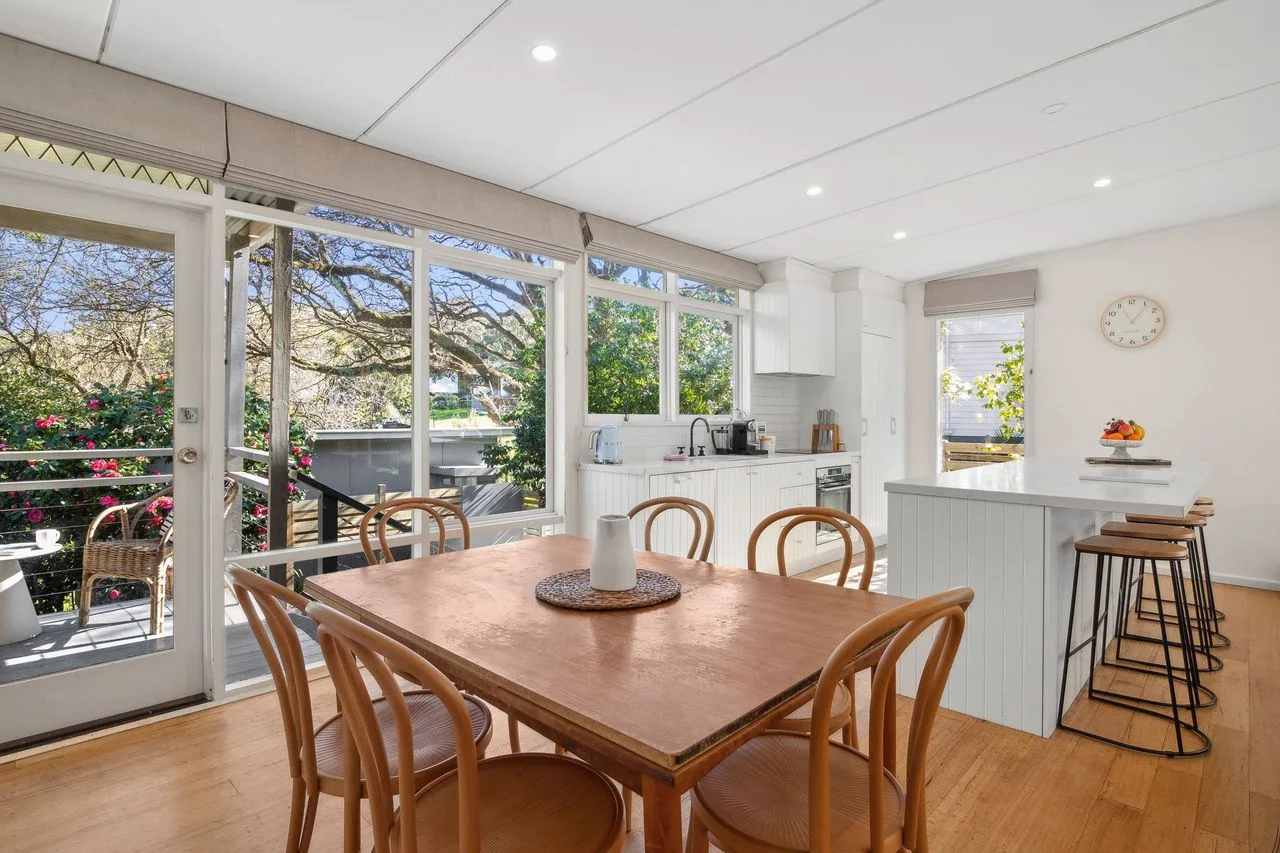 A bright kitchen and dining area with a wooden table beside large windows.