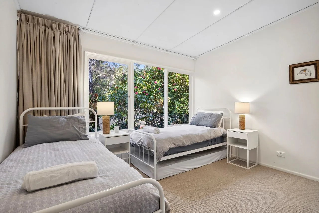 A bedroom with two single beds beside large windows overlooking greenery.