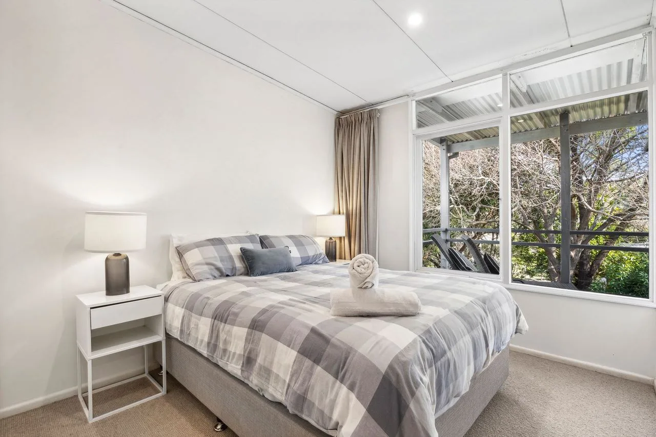 Bedroom with a bed beside large windows overlooking trees.
