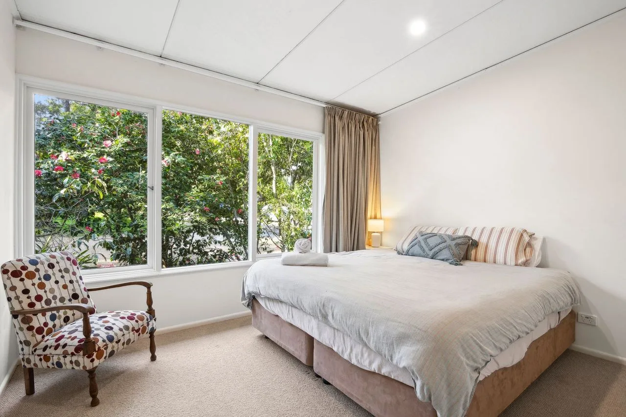 A bright bedroom with a large bed beside wide windows overlooking greenery.