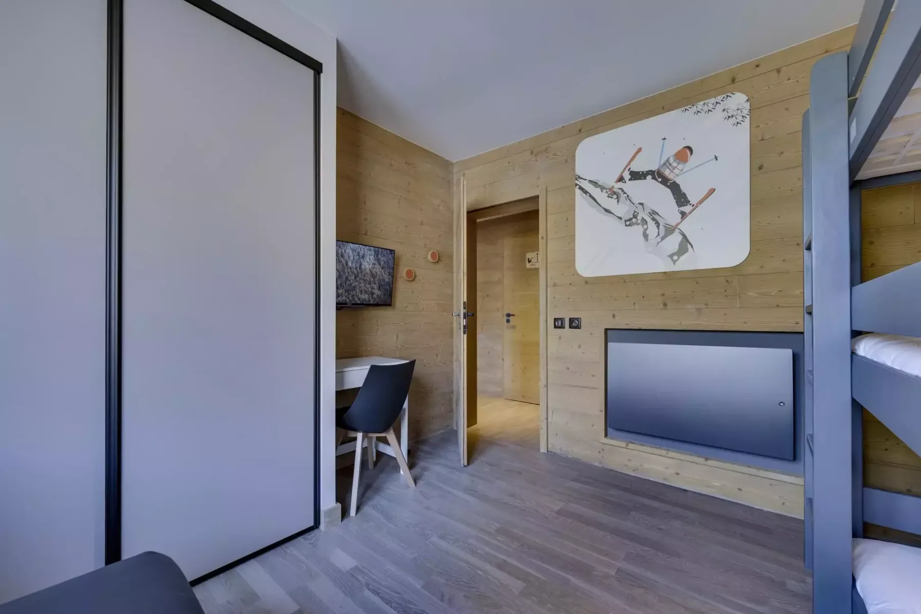 A wood-paneled bedroom with bunk beds, a desk, and a wall-mounted screen.