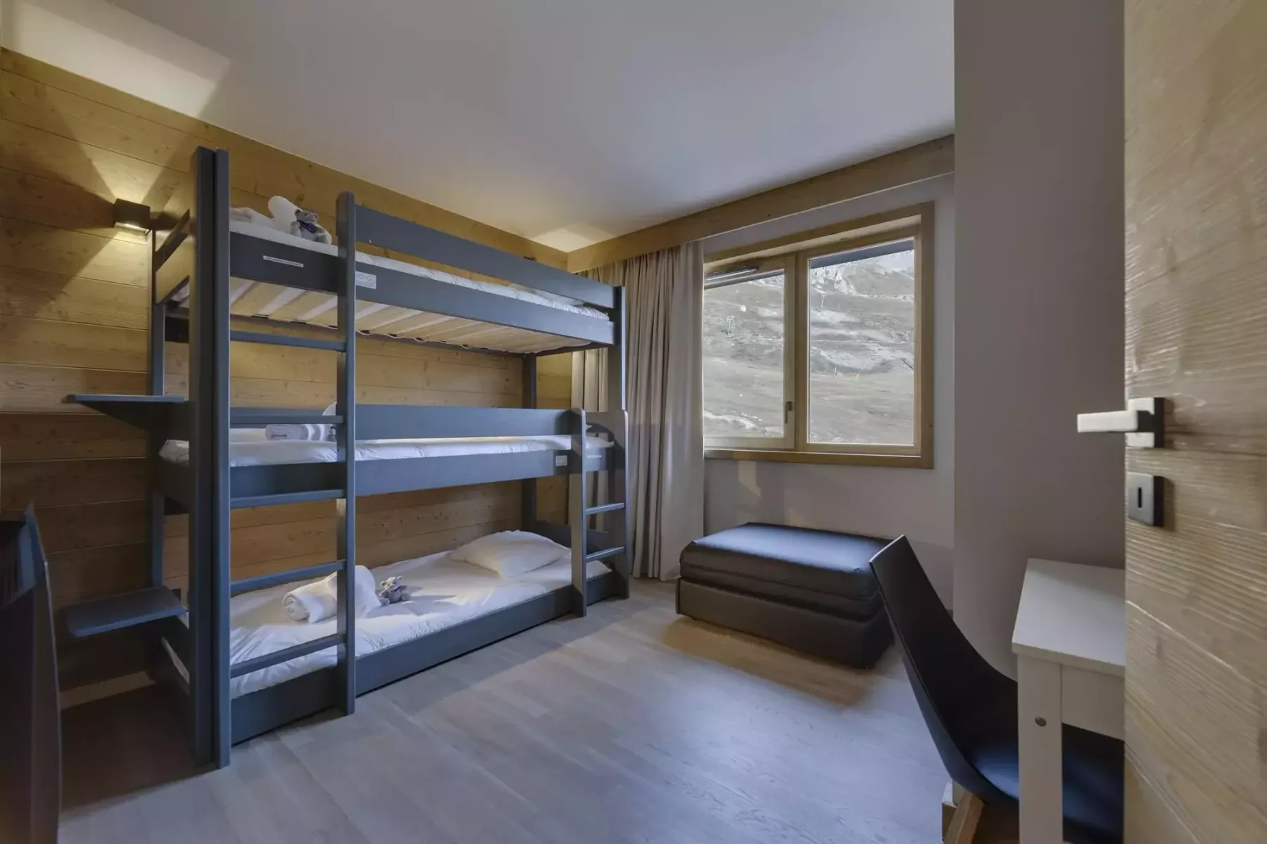 A bedroom with a metal bunk bed and a window overlooking a snowy landscape.