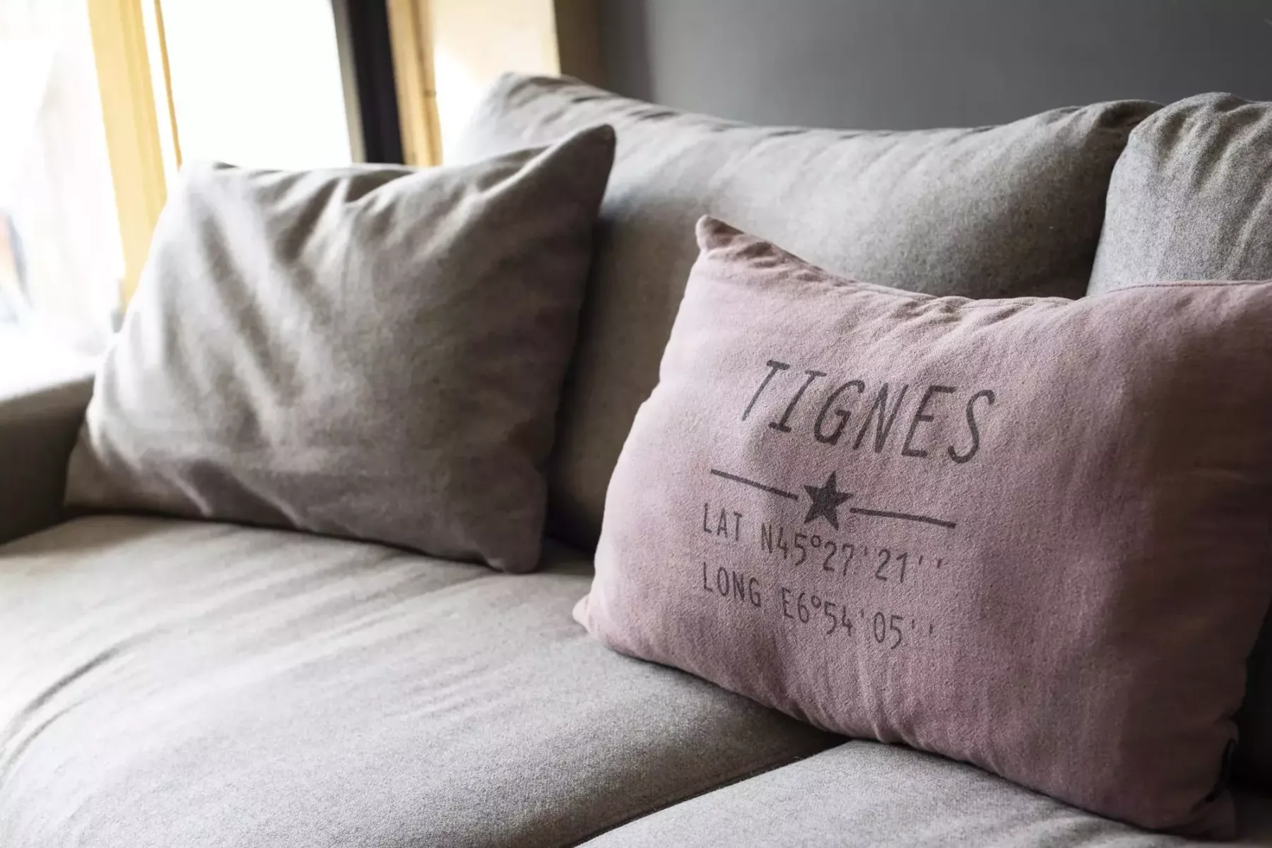 A gray sofa with two cushions, including a mauve cushion printed with text.