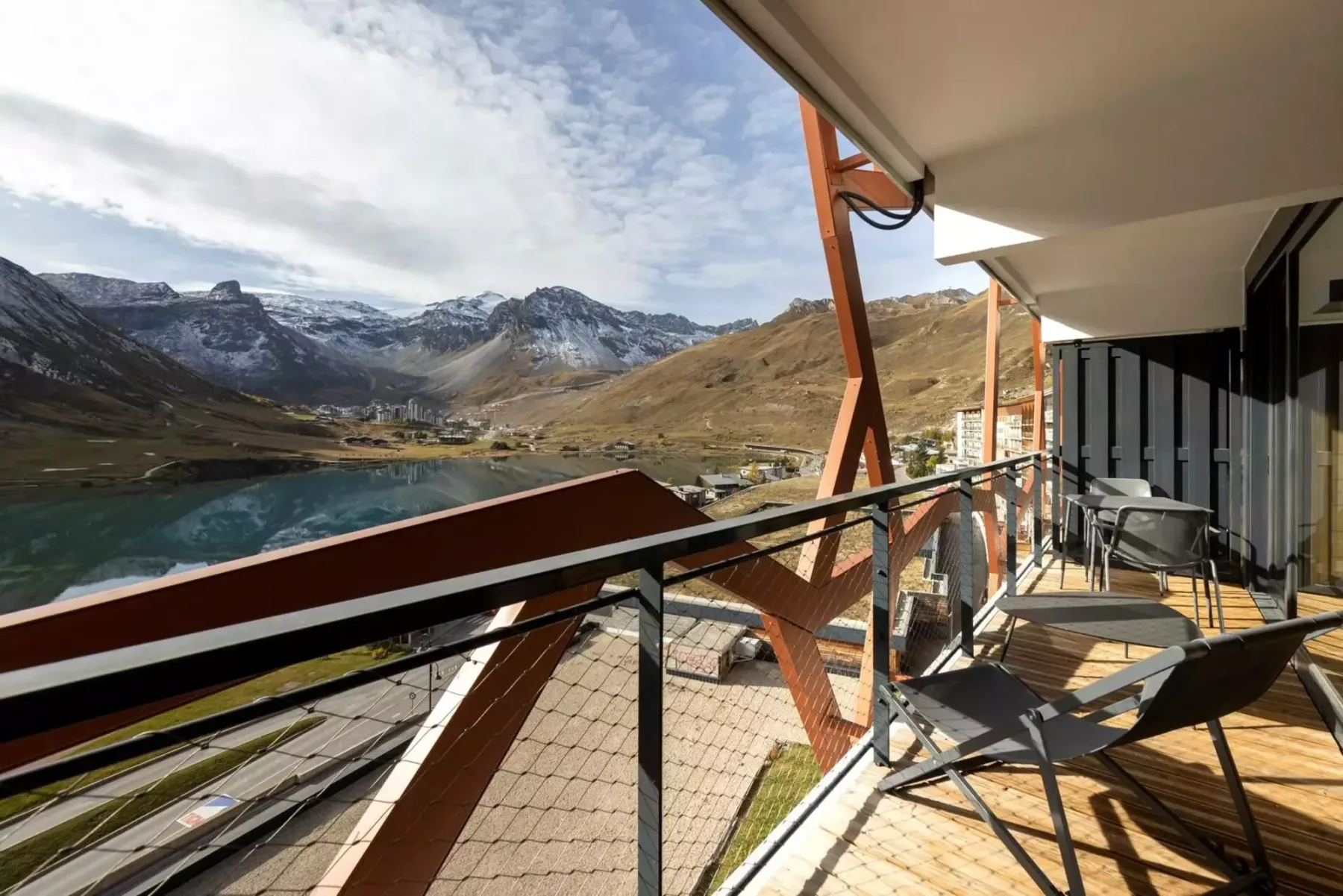 A balcony with seating overlooks a lake and mountain valley.