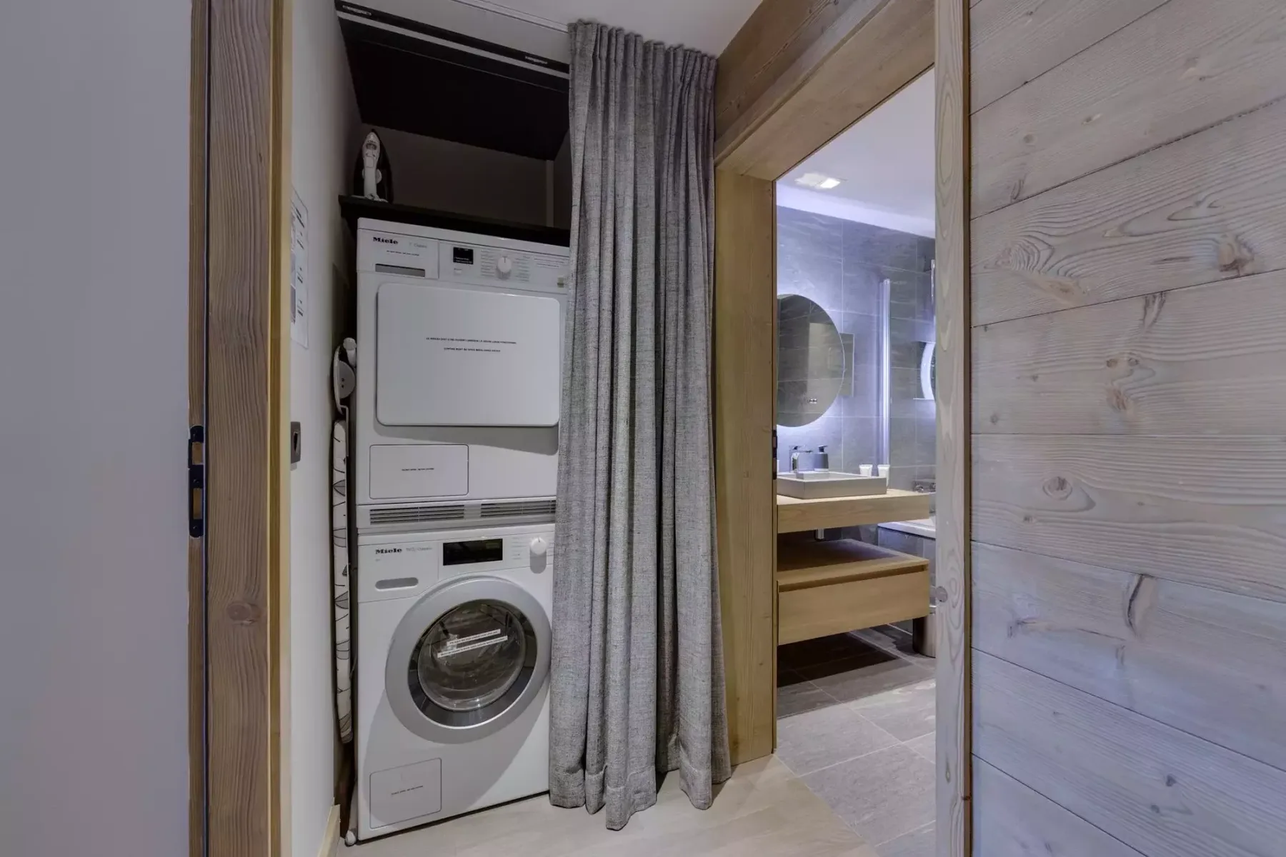 A laundry area with a stacked washer and dryer beside a curtained bathroom doorway.