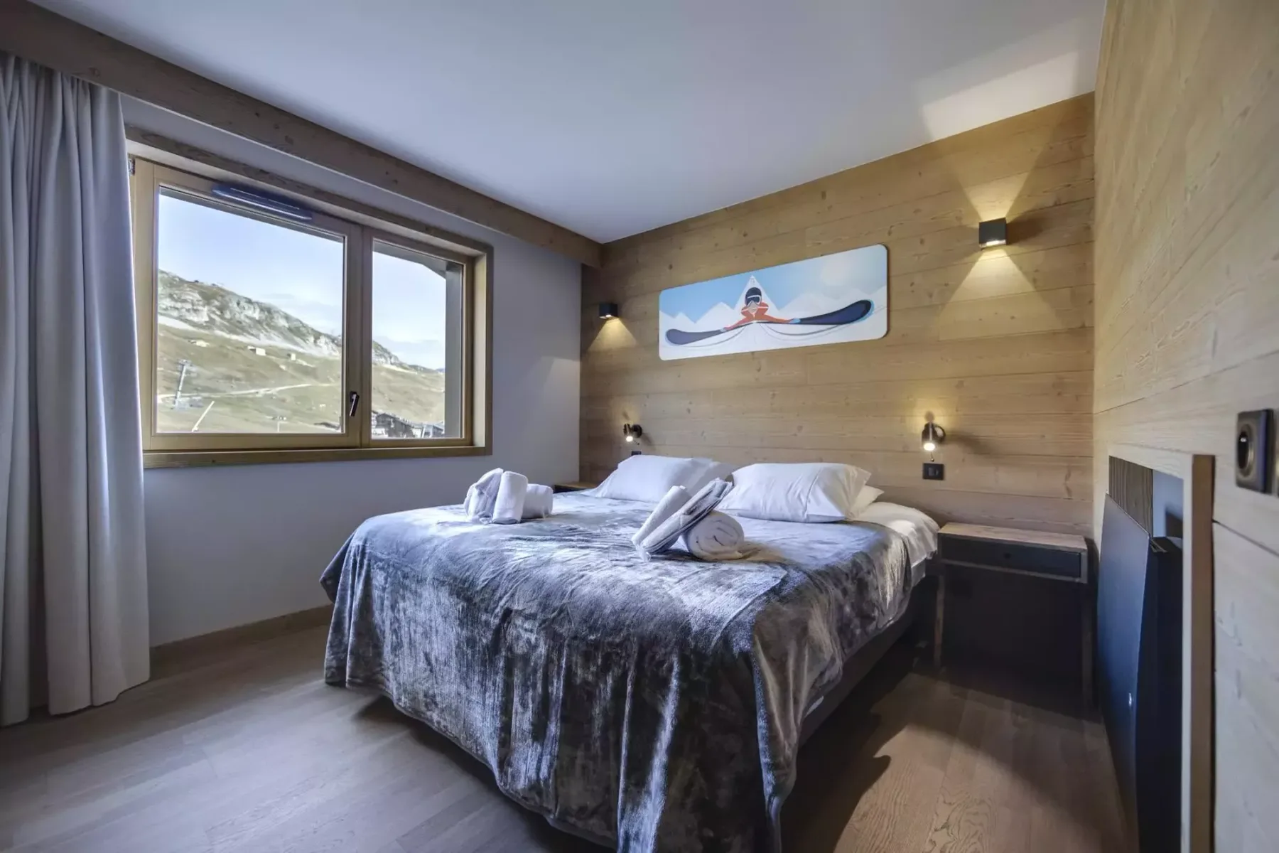 A bedroom with two beds, a large window, and a wooden accent wall.