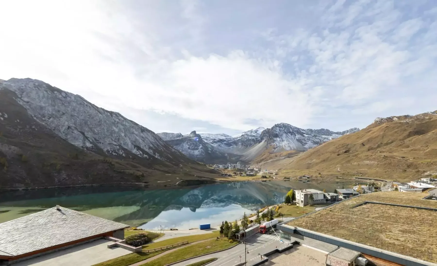 A mountain lake reflects the surrounding peaks beside a small cluster of buildings.