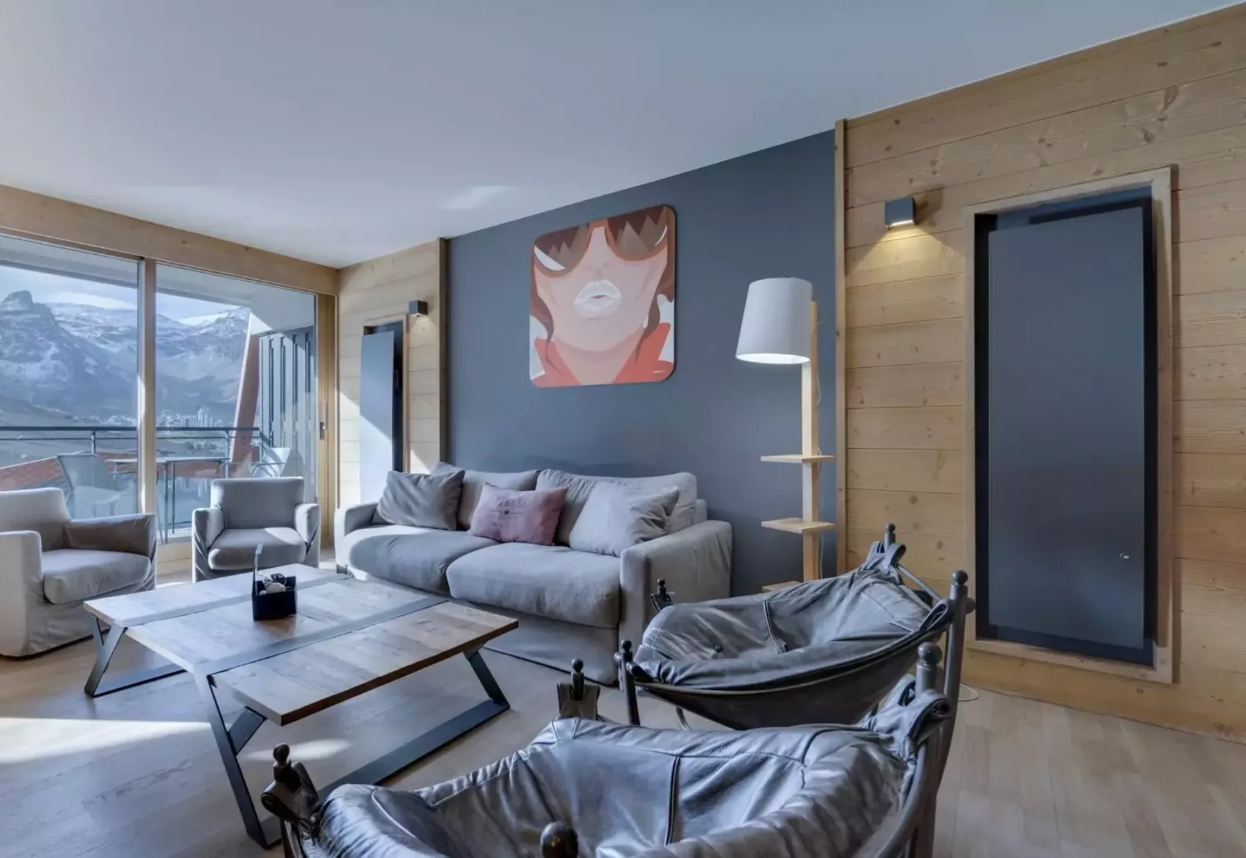A living room with a gray seating area, coffee table, and large windows overlooking mountains.