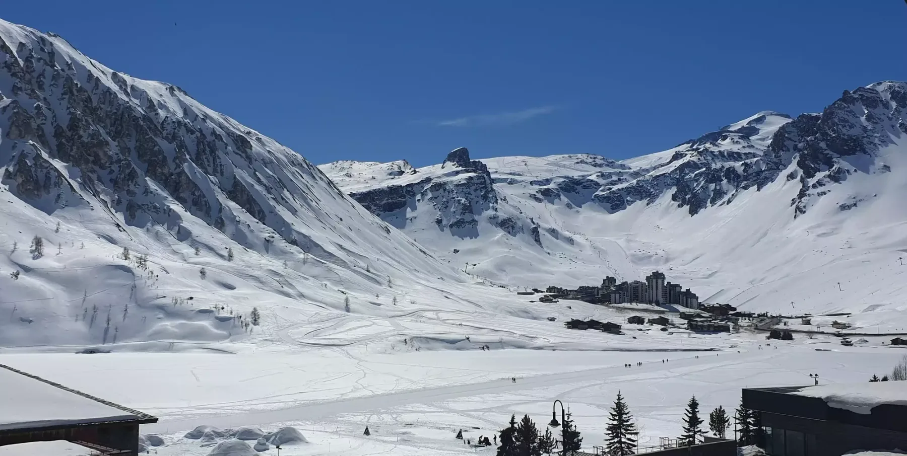 A snow-covered mountain valley stretches beneath a clear blue sky.