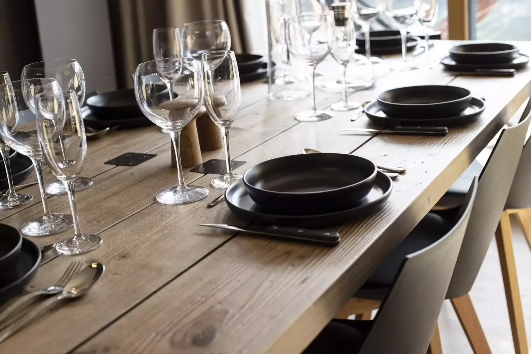 A dining table is set with dark plates, cutlery, and wine glasses.