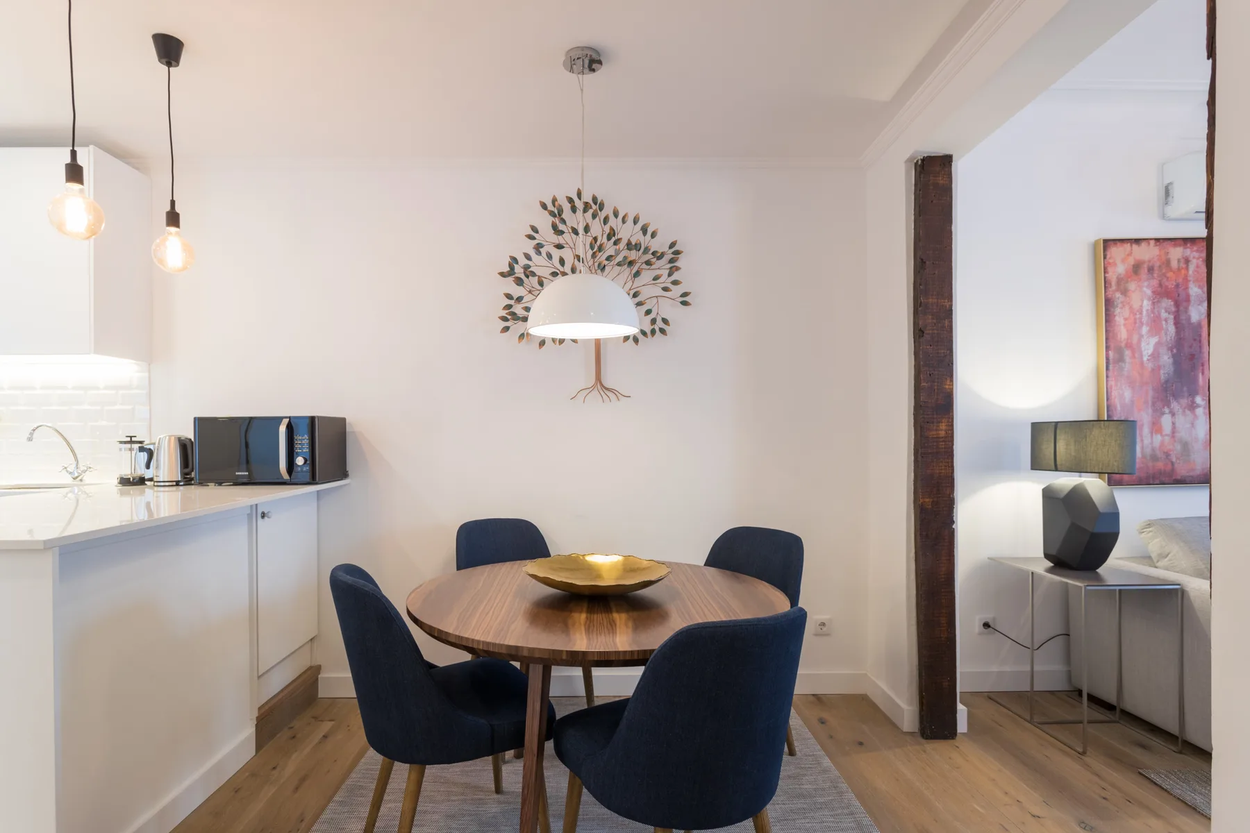Comedor con una mesa redonda de madera y asientos tapizados oscuros junto a la cocina.