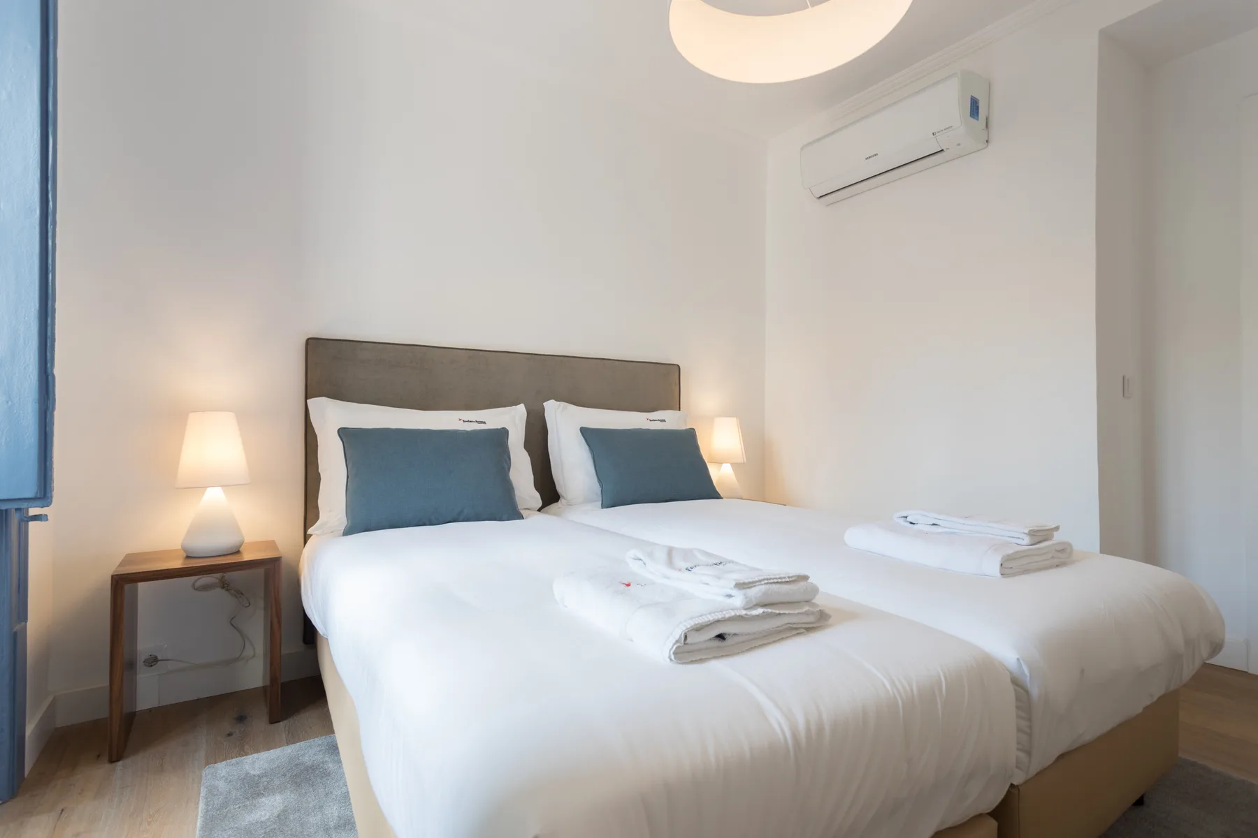 Un dormitorio con dos camas, mesitas de noche y un aire acondicionado en la pared.