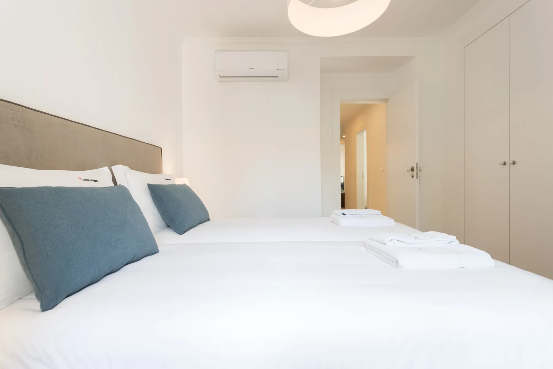 Un dormitorio luminoso con ropa de cama blanca, almohadas azules y armarios empotrados.