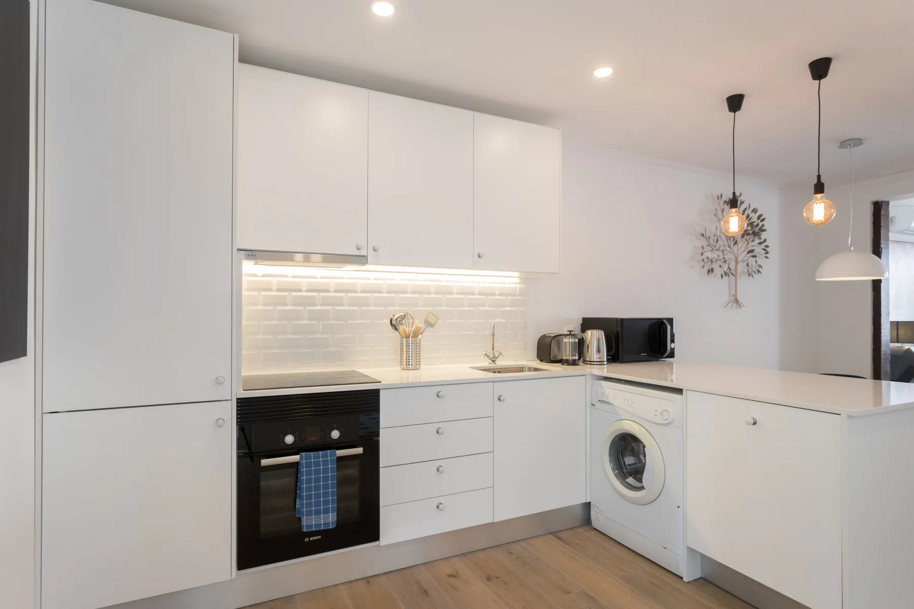 Cocina moderna con muebles blancos, horno empotrado y lavadora.