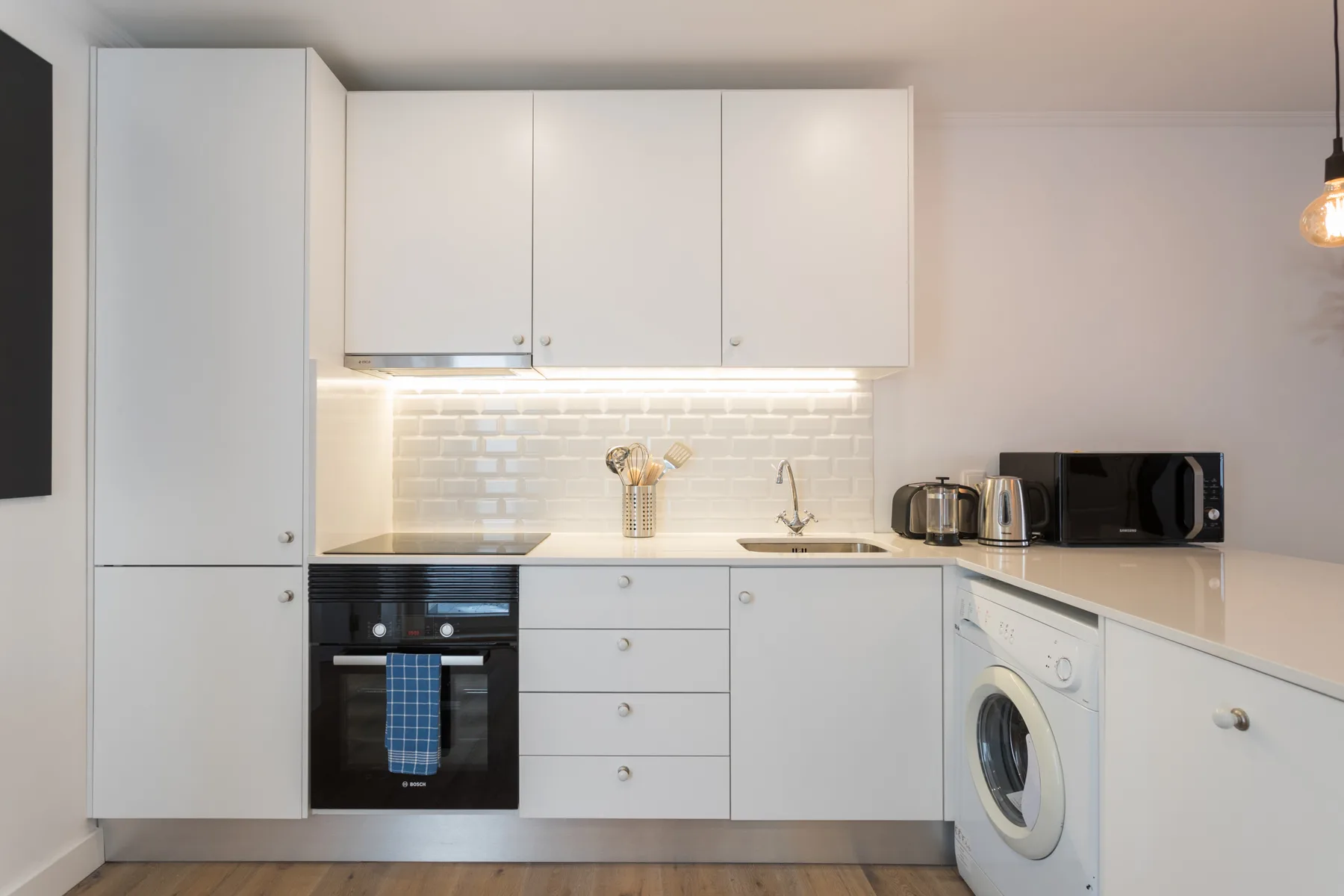 Una cocina moderna con armarios blancos, una placa de cocina y una lavadora.