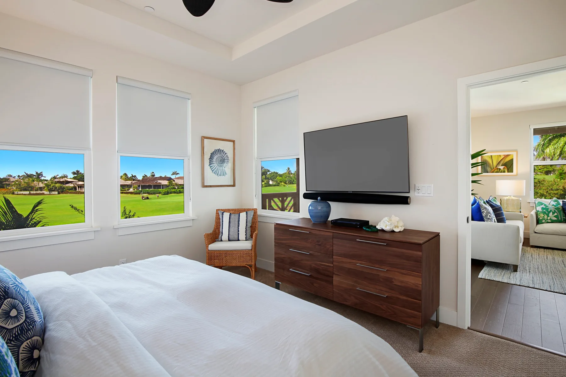 Un dormitorio luminoso con una cama, una cómoda de madera y un televisor montado en la pared.