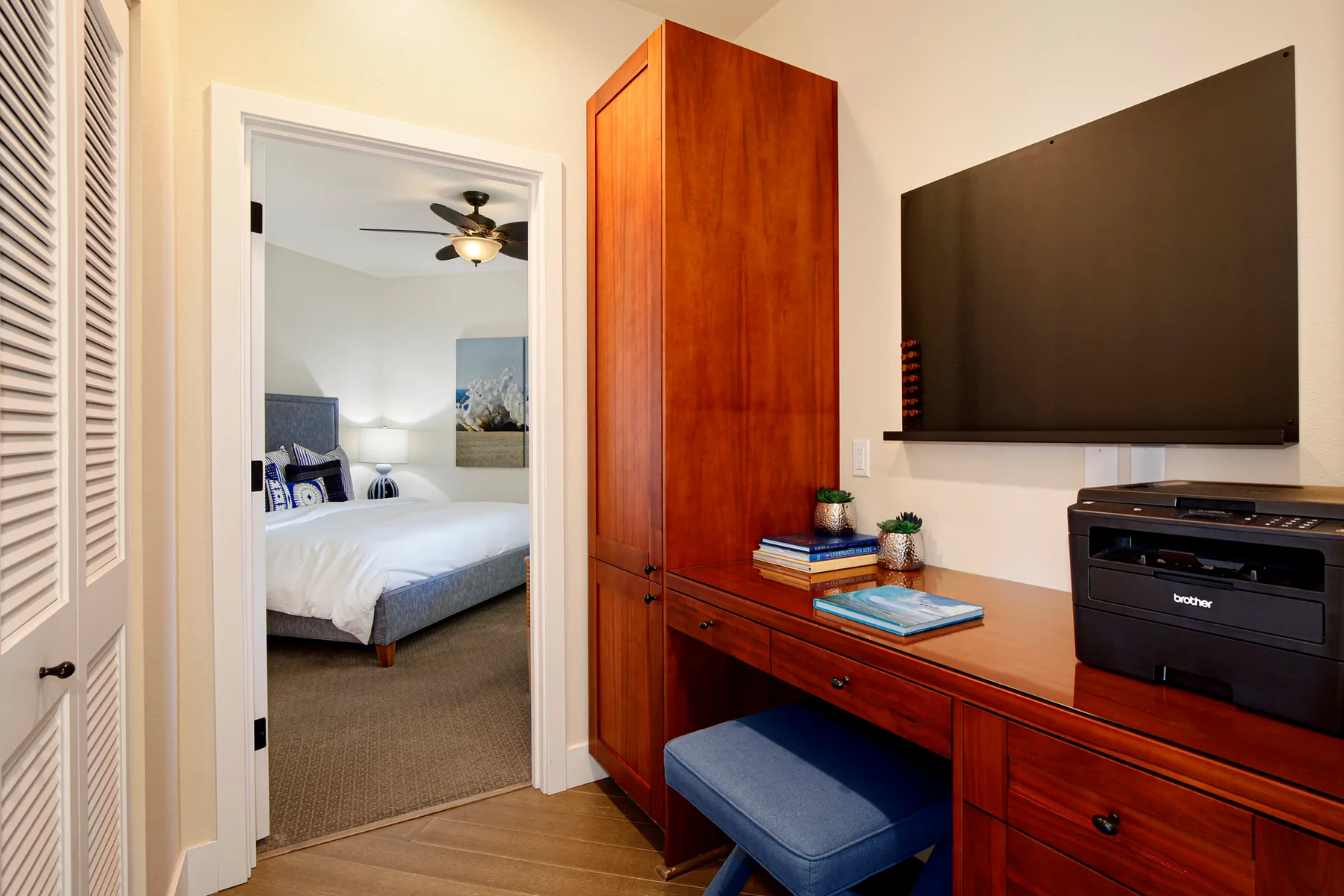 Una puerta da a un dormitorio junto a un escritorio de madera y un televisor montado en la pared.