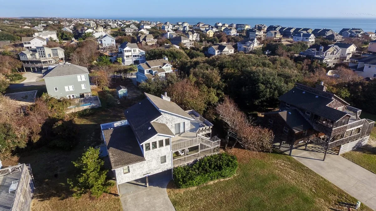 An aerial view of a coastal neighborhood with houses and the ocean in the distance.