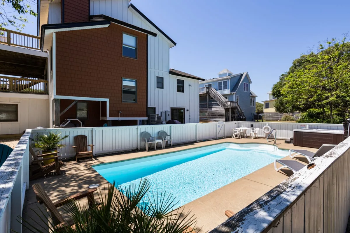 An outdoor swimming pool sits beside modern multi-story buildings and patio seating.