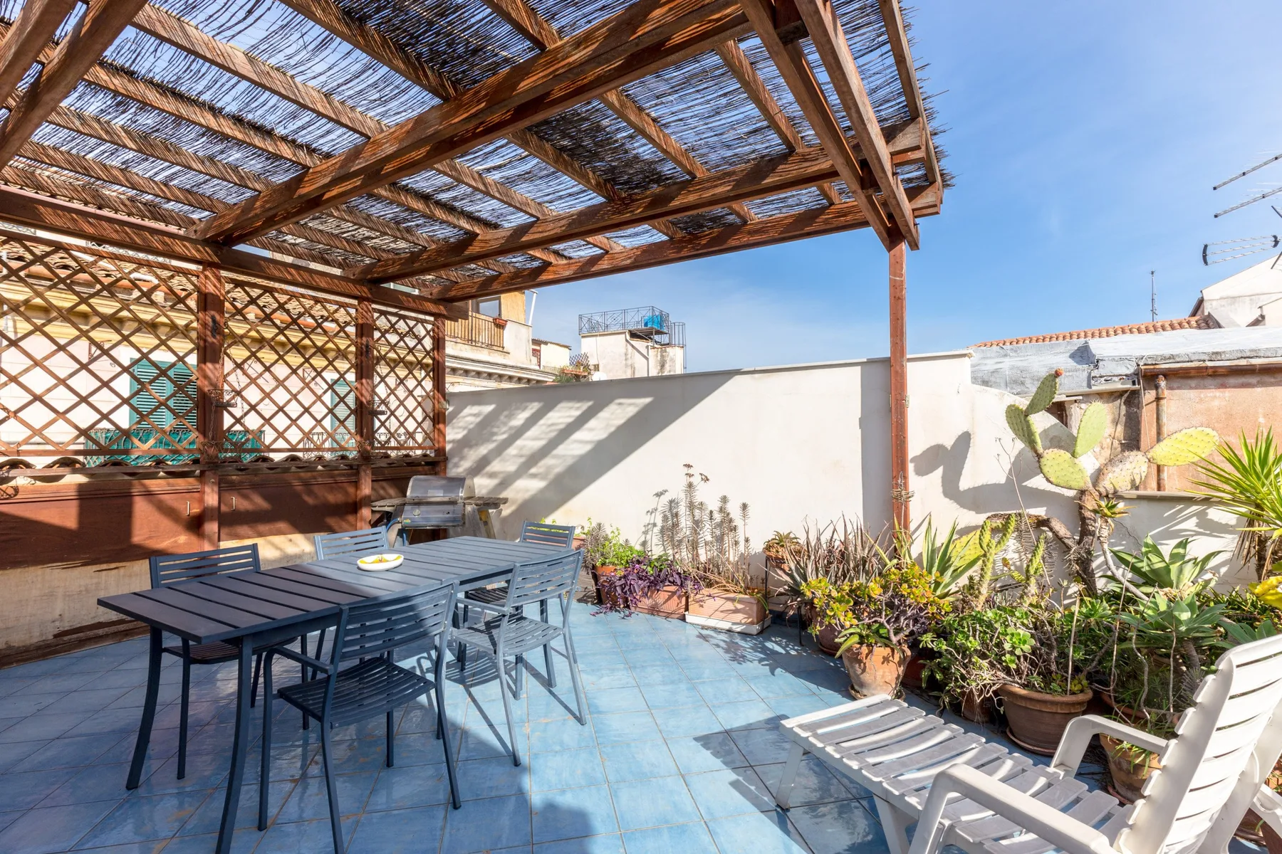 Una terraza soleada en la azotea con asientos al aire libre, plantas en macetas y una pérgola de madera.