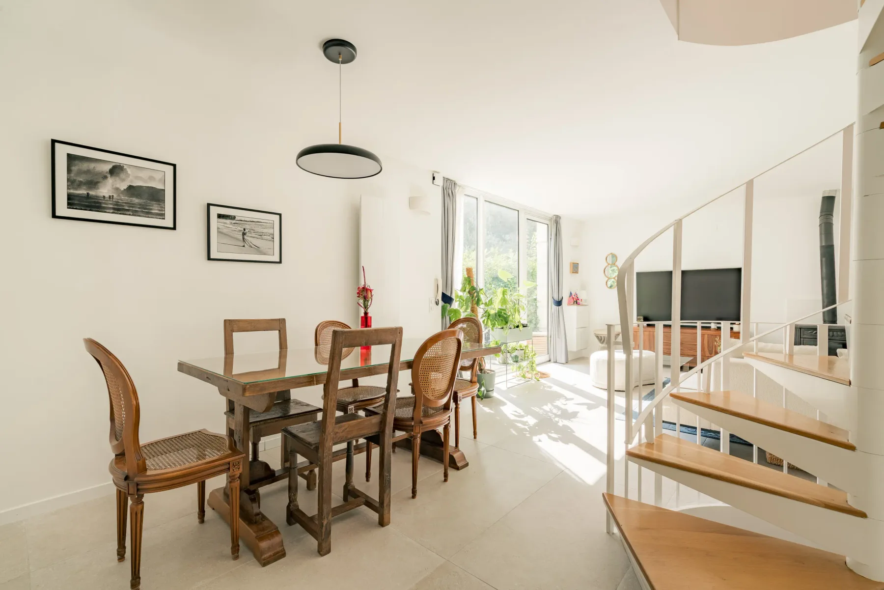 A bright dining and living area with a wooden table beside the staircase.