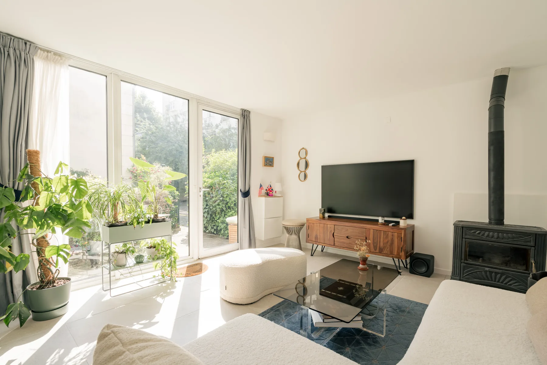 A bright living room with large windows, plants, and a television.