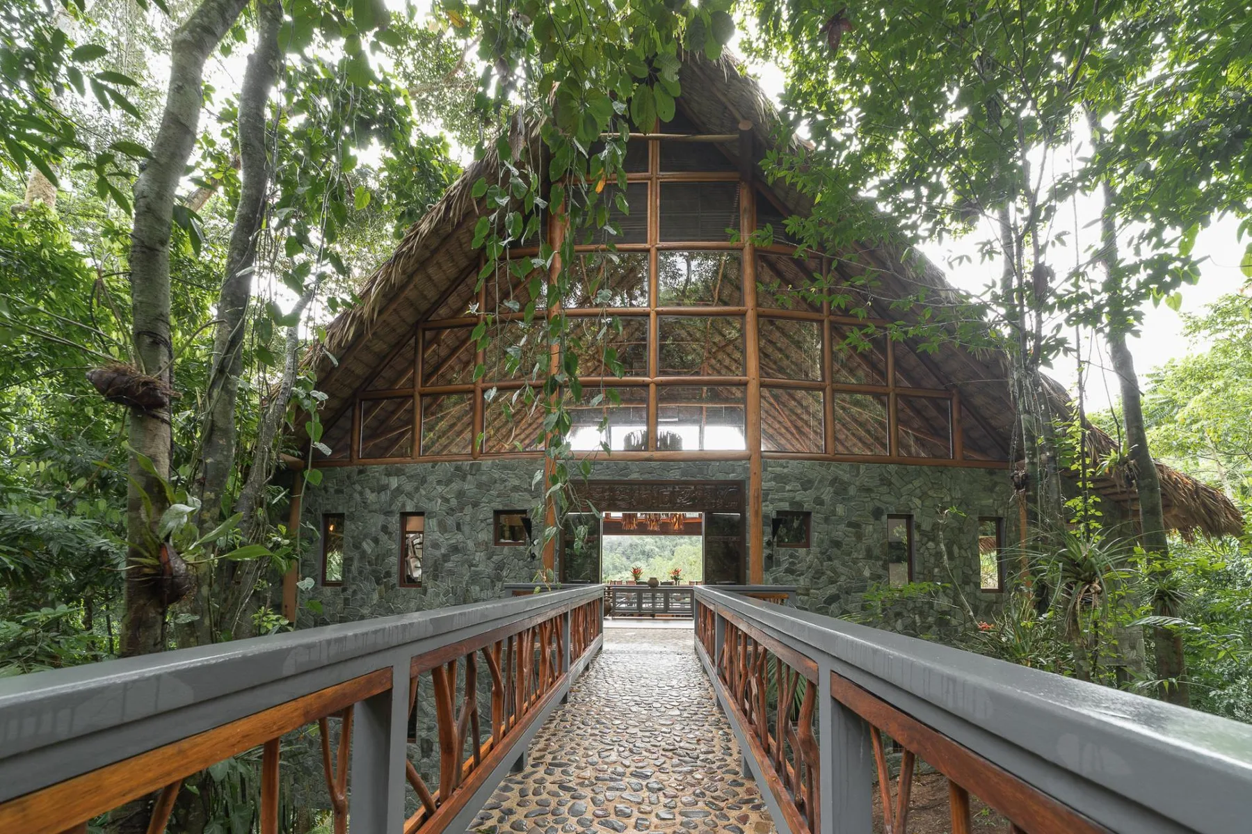 A forest lodge with a stone facade and a raised walkway leading to its entrance.