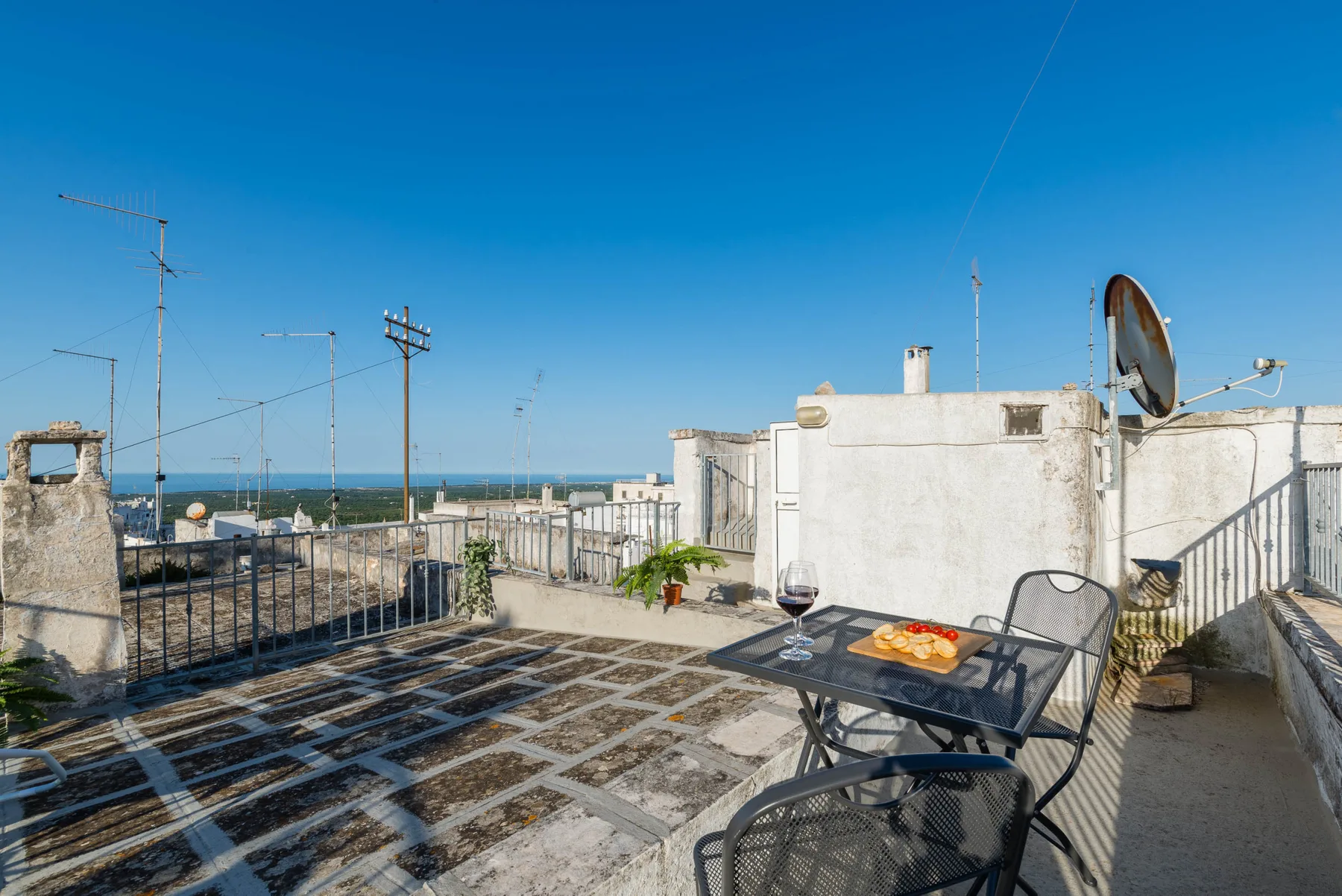 A rooftop terrace has a dining table and chairs overlooking the sea.
