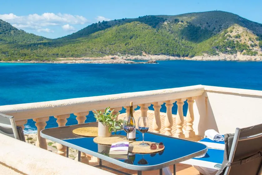 A terrace dining table overlooks blue water and a green hillside.
