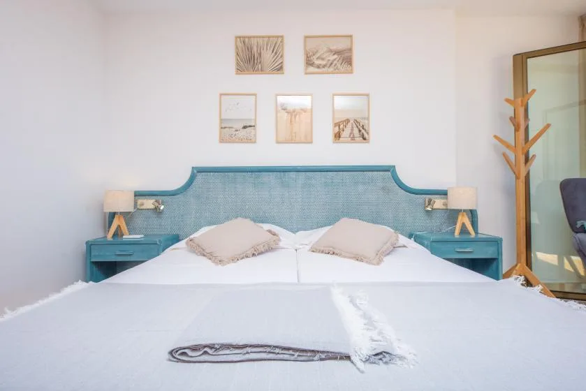 A bedroom with a neatly made bed, turquoise headboard, and framed artwork.