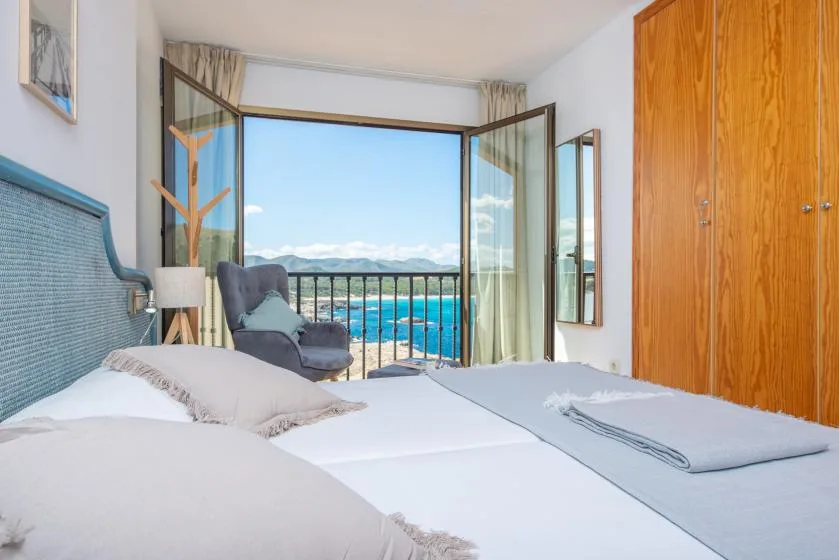 A bedroom with beds beside open doors overlooking a balcony and distant mountains.