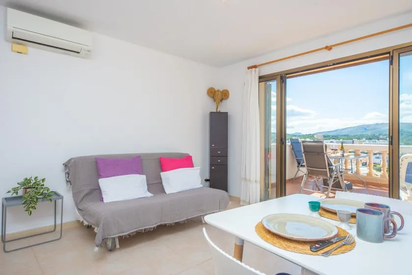 A bright living room opens onto a balcony, with a sofa and dining table.