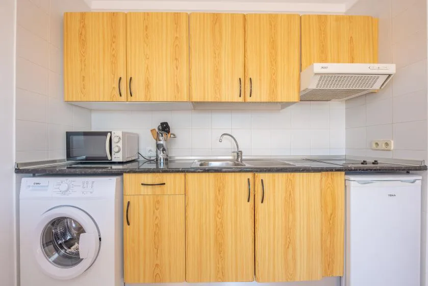 A compact kitchen with wooden cabinets, a sink, and a washing machine.