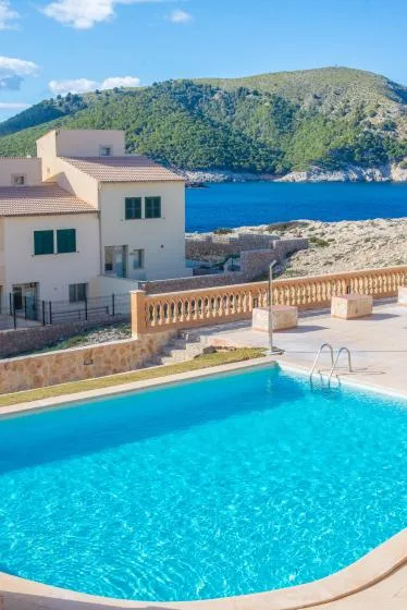 A swimming pool overlooks a blue bay and a green hillside.