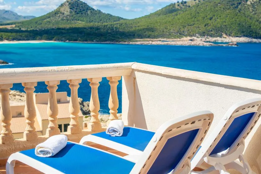 A sunlit terrace with blue lounge seating overlooking the sea and green hills.