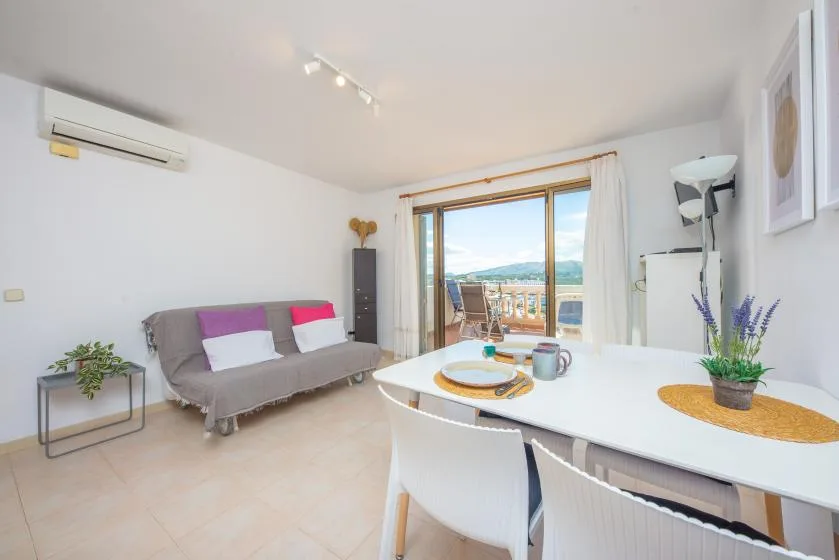 A bright living and dining area with seating, a table, and windows overlooking the water.