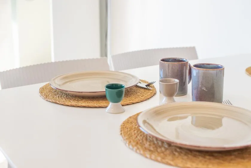 A dining table is set with plates, woven placemats, and cups.