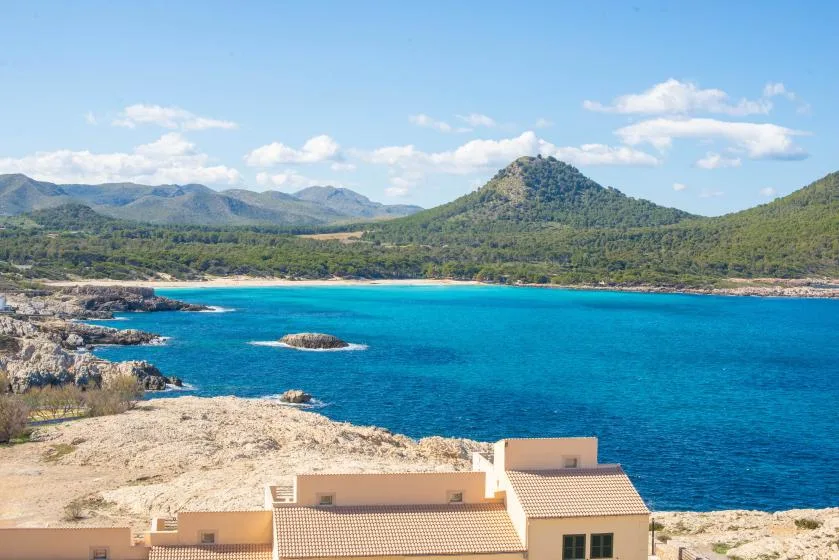 A coastal bay with blue water, rocky shoreline, and green hills beyond.