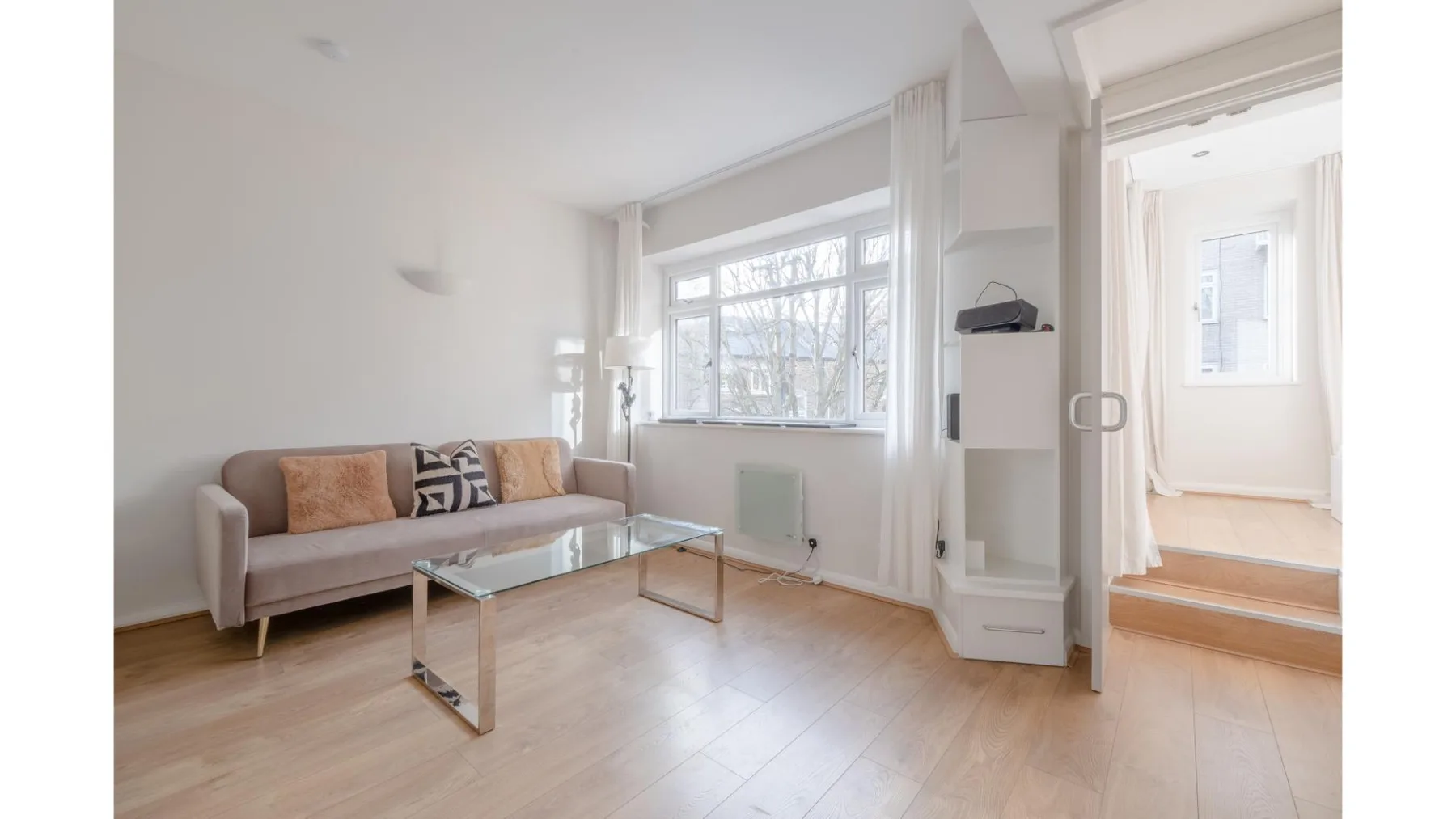 A bright living room with seating, a glass coffee table, and large windows.