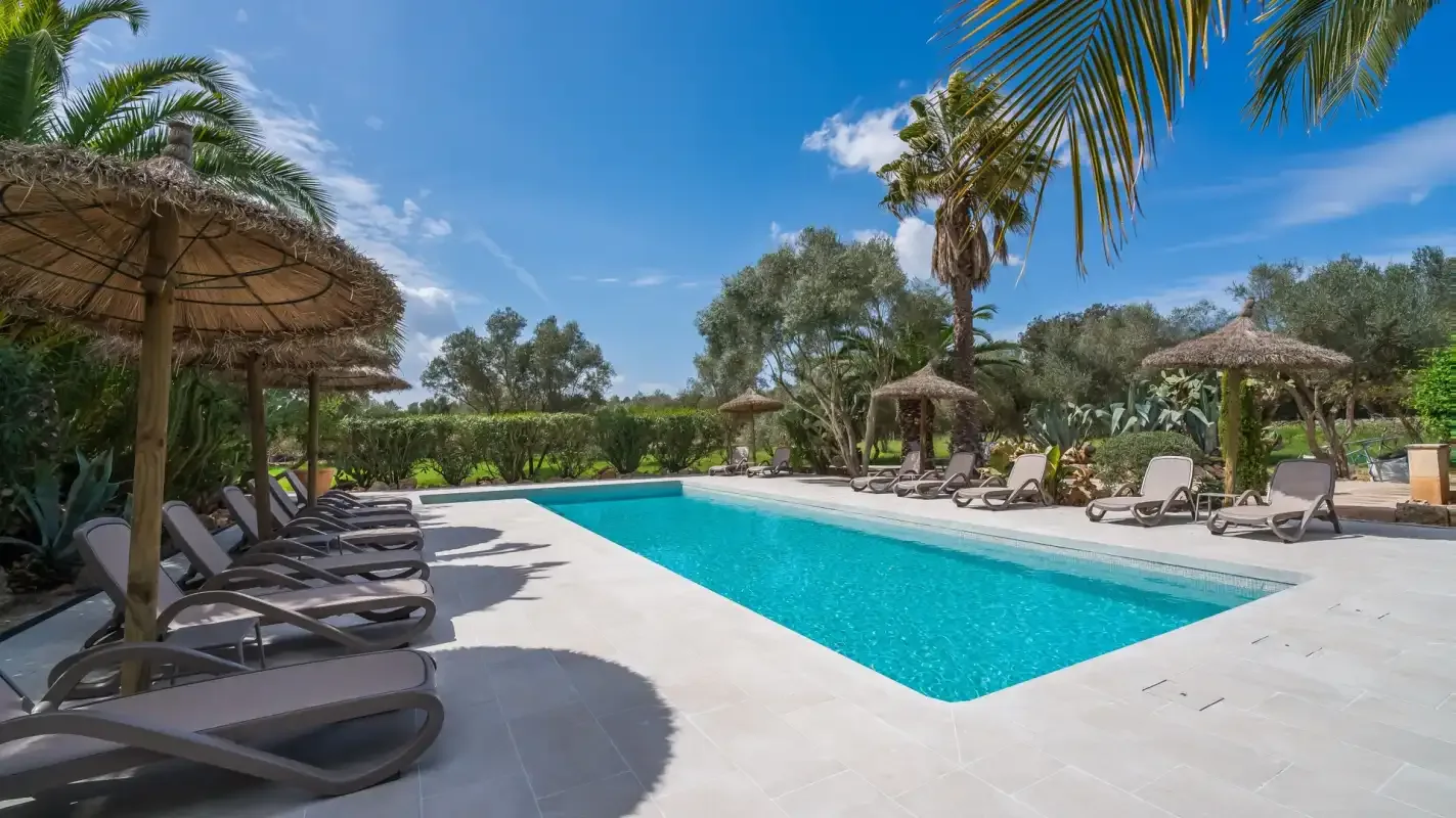An outdoor swimming pool is surrounded by sun loungers and shaded seating.