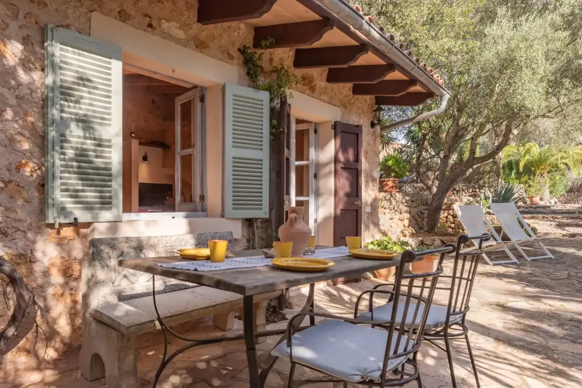 An outdoor dining area beside a stone house, with open windows and patio seating.