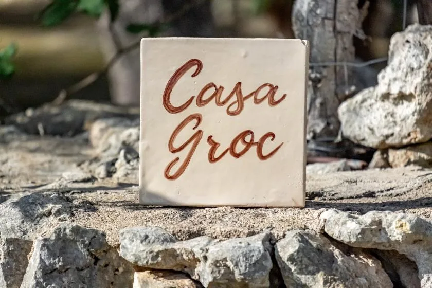 A ceramic sign reading “Casa Groc” rests on a low stone wall.