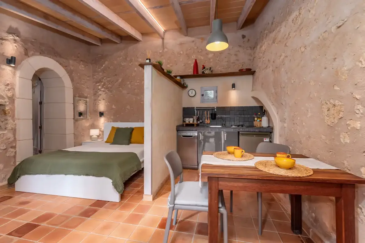 A rustic studio room combines a bed, dining table, and compact kitchen.