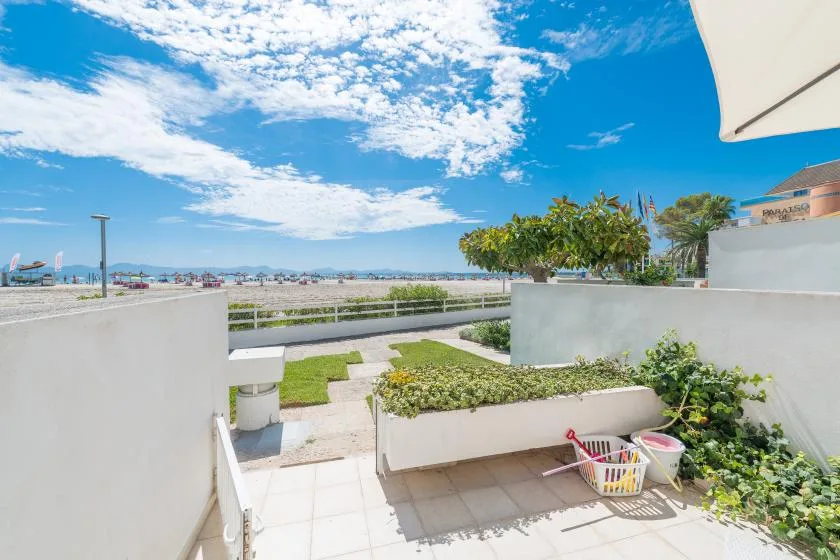 Una terraza soleada con patio de baldosas, jardineras elevadas y vistas al mar.