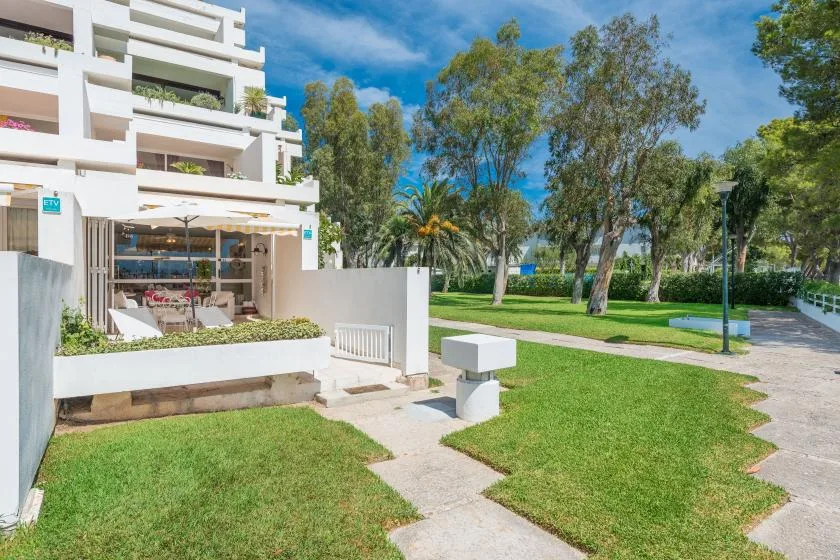 A white apartment building beside a landscaped lawn and paved walkway.